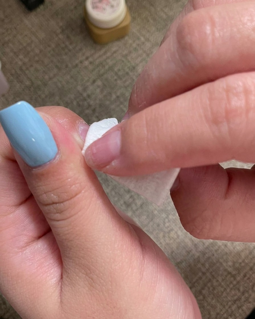 毛羽立たないワイプを使って、マニキュアを塗った爪の表面を綺麗に拭き取っている手。