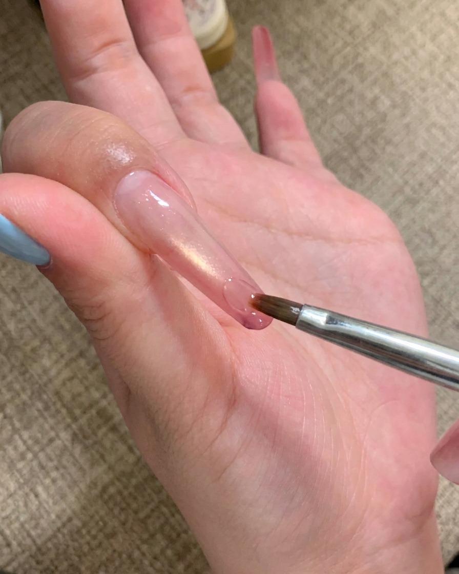 細筆を使って、長い爪の先端にクリアなアドヒシブジェルを少量塗っている様子。