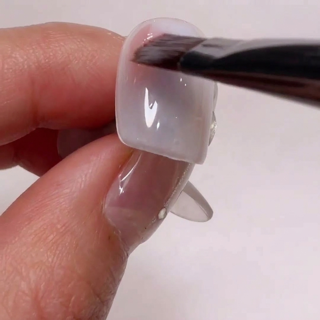 ネイルチップの角に柔らかいヌードピンクのジェルをブラシで塗っている様子。