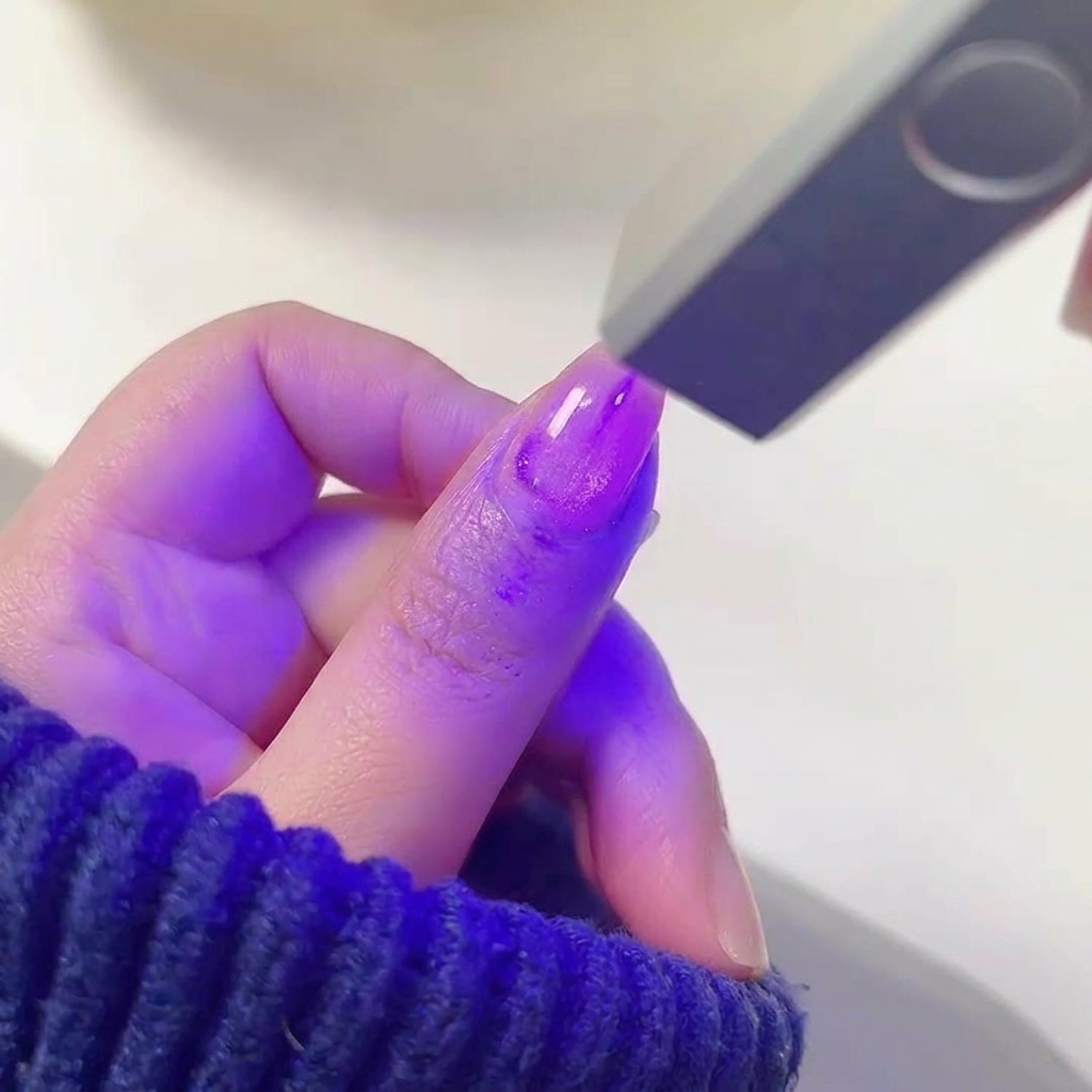 きらめくパープルのジェルが塗られた爪を、光るUV/LEDネイルランプの中に入れている様子。