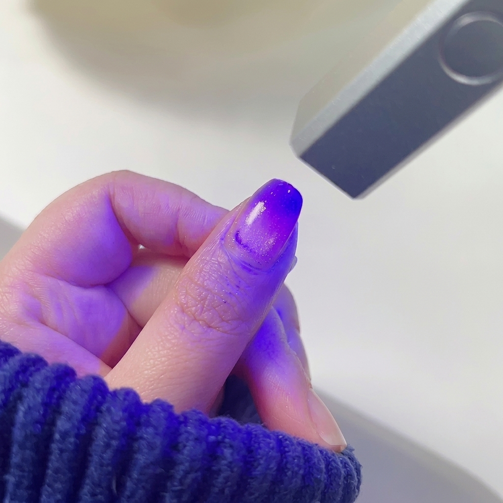 ピンクとパープルのグラデーションが施された親指の爪を、小型LEDランプで硬化している様子。