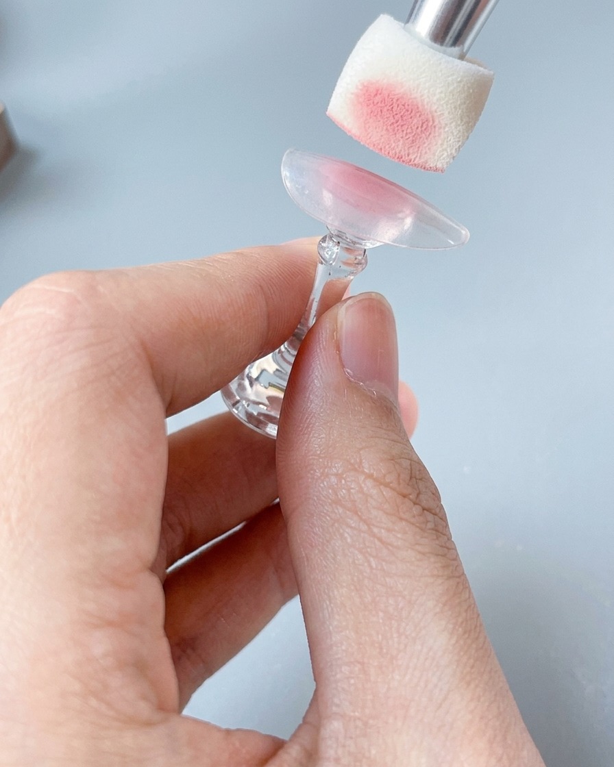 ネイルスタンドに固定されたネイルチップに、スポンジツールで柔らかいチークピンクを塗布している様子。