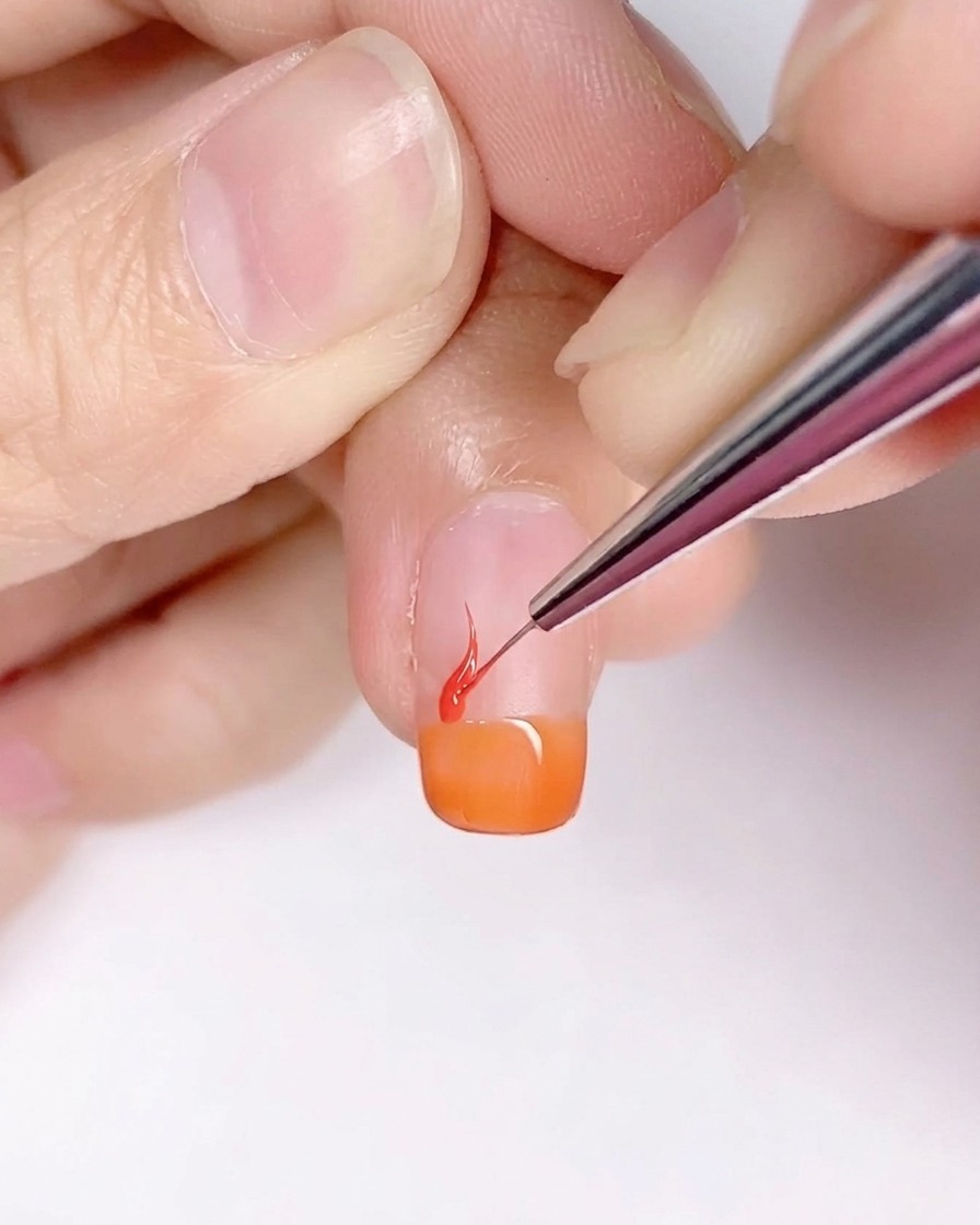 細いライナー筆を使って、オレンジのベースの上に炎のような形を描いている様子。