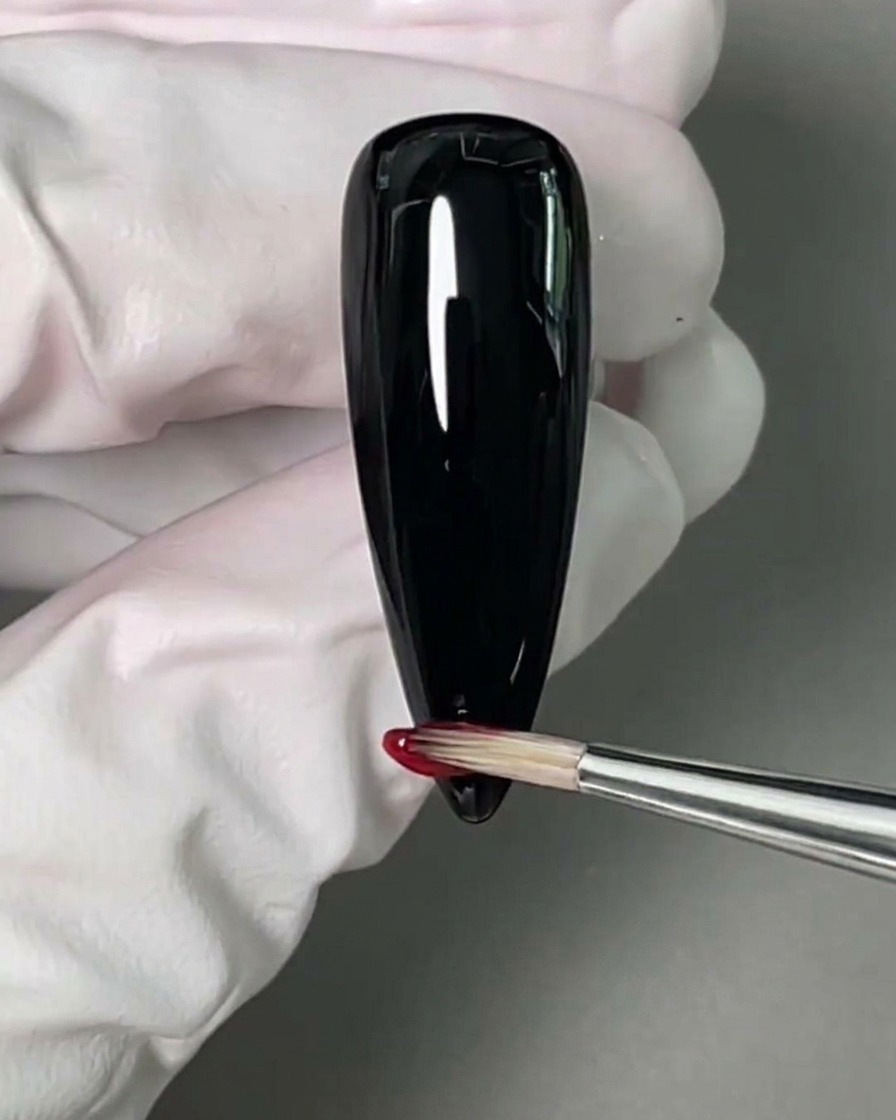 黒く塗った爪の先に、赤いジェルポリッシュを乗せている様子