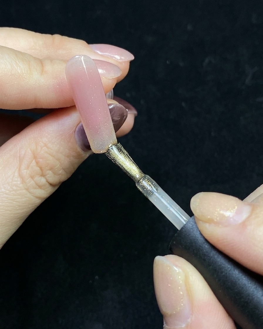 ヌードベースのネイルの先端にゴールドのキャットアイジェルを塗っている様子。
