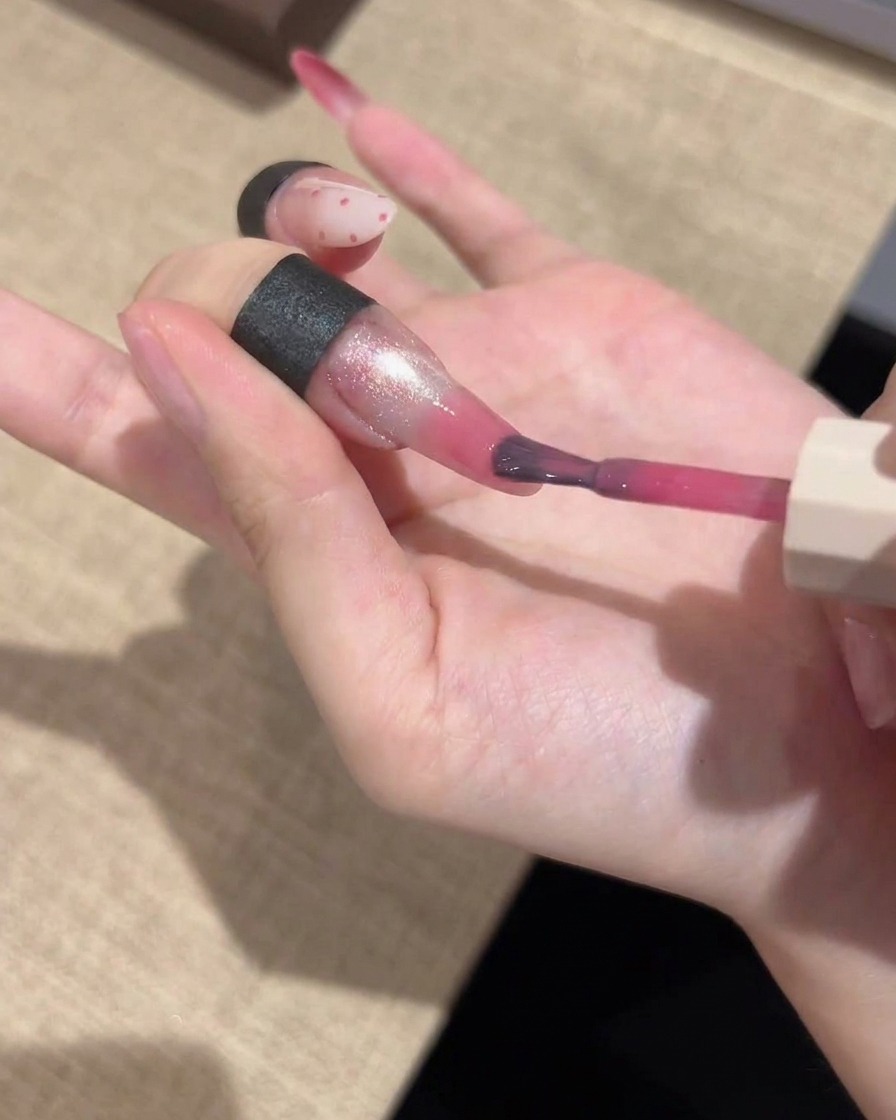 細筆を使って鮮やかなピンクのジェルを爪の先端に塗り、グラデーションになるようになじませている様子。