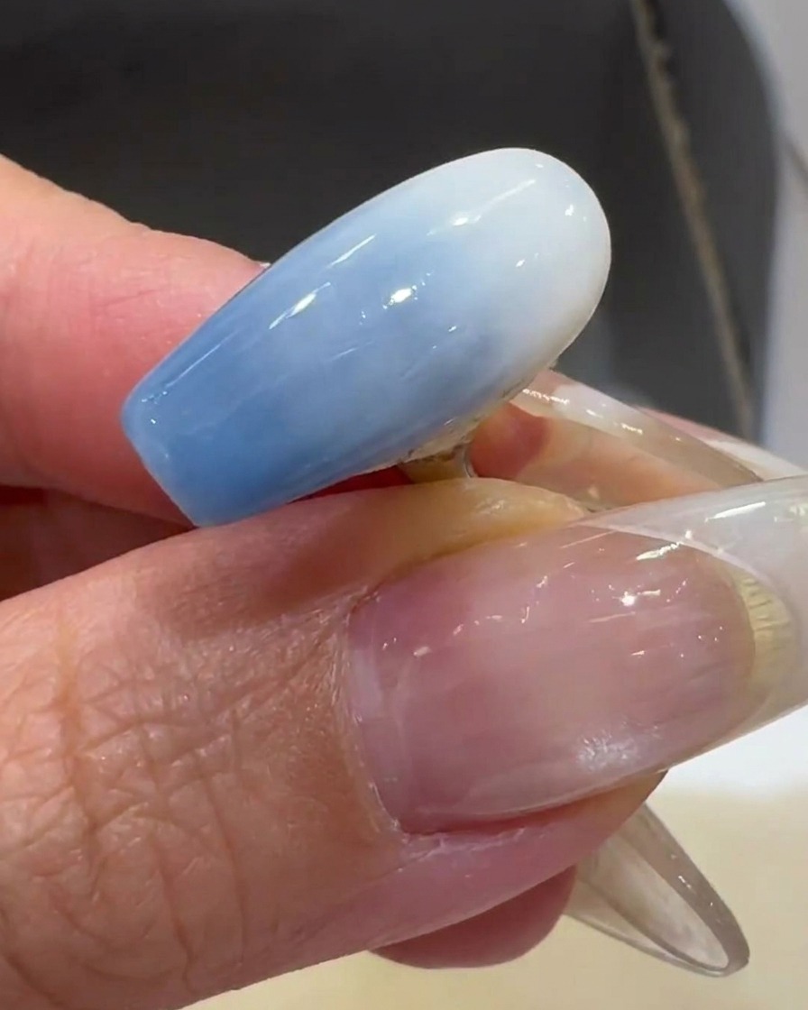 クリアなネイルチップにミルキーホワイトのジェルを薄く塗っている様子。