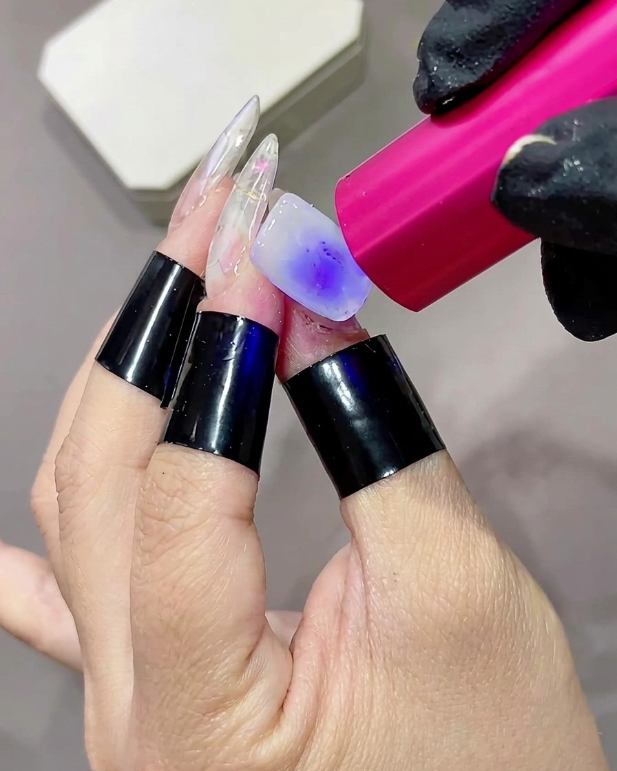 ミルキーホワイトのベースジェルを塗った指を、ピンク色の小型ハンディUV/LEDランプで硬化しているクローズアップ画像。
