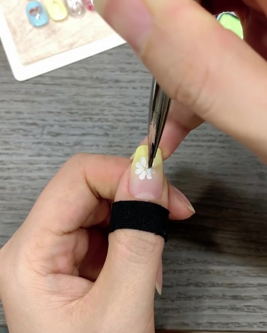 細筆を使って、白いデイジーの中心に鮮やかなイエローの小さな点をのせている様子。