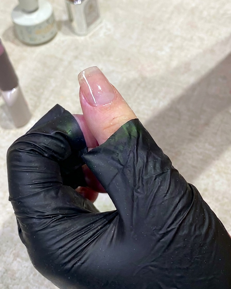 手がUVネイルランプの中に入り、ライトが点灯してベースジェルを硬化している様子。