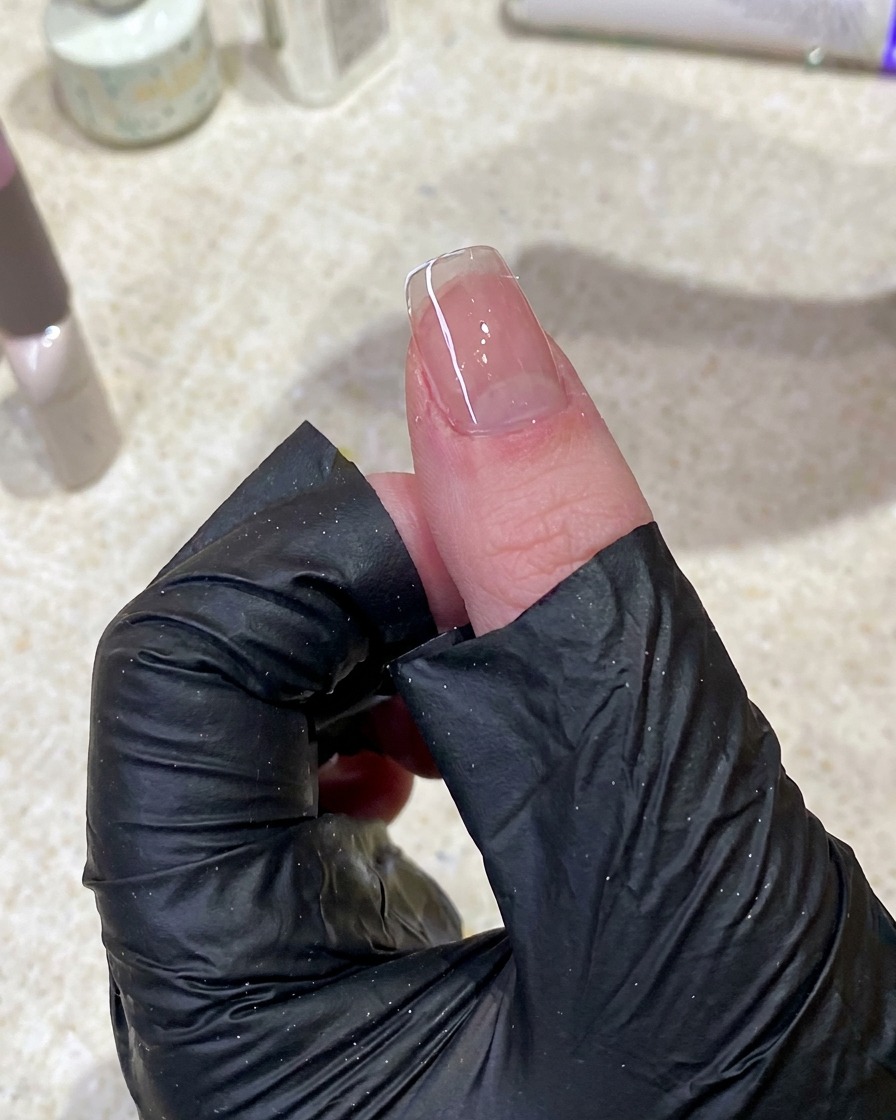 手袋をした手が、糸くずの出ないワイプを使ってネイル表面の未硬化ジェルを拭き取っているクローズアップ写真。