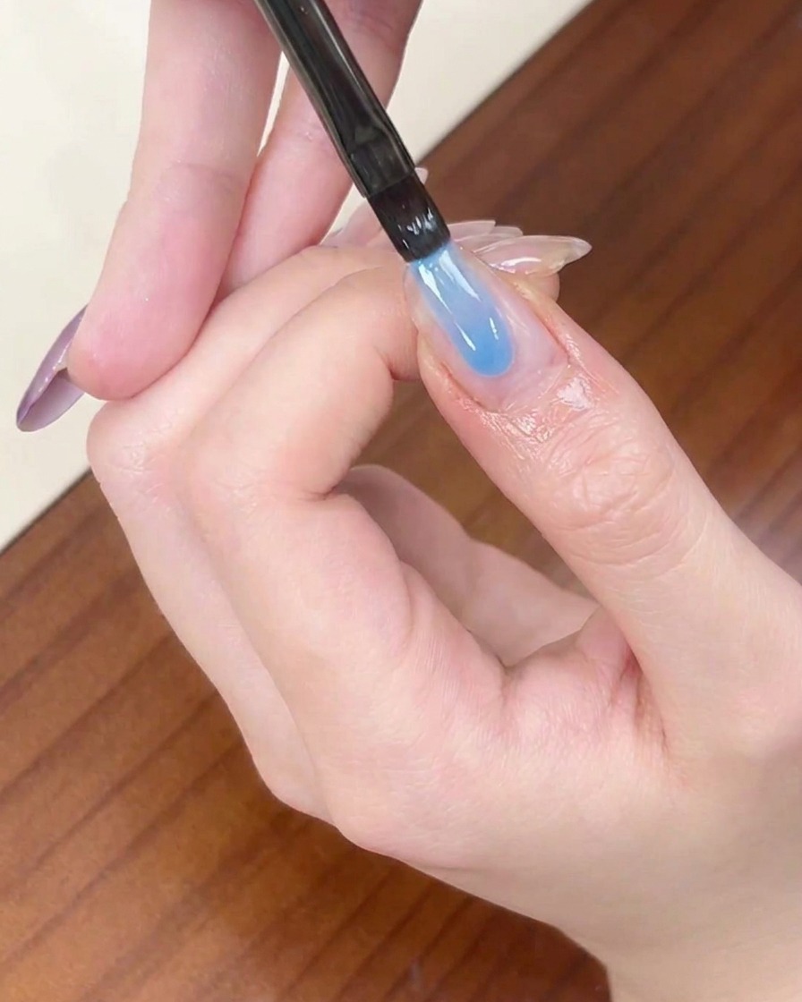 ライナーブラシを使い、アーモンド型の爪の先端に透明感のあるブルーのジェルを塗布している様子。