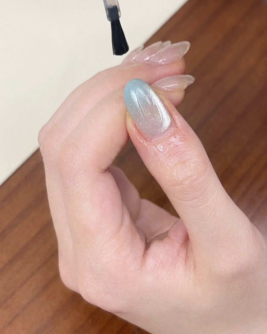 ブルーのキャットアイネイルの上に、ツヤのあるクリアトップコートを塗っている様子。
