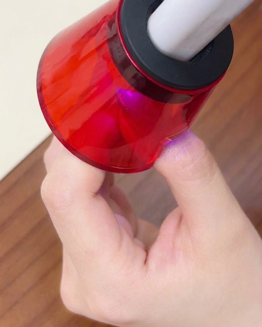 小型の赤いポータブルUV/LEDライトで、最終仕上げの硬化をしている様子。