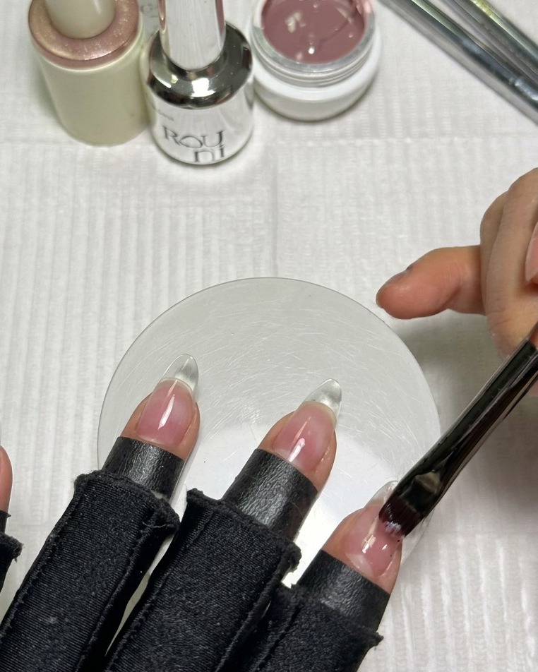 アーモンド形のクリアネイルチップに、ピンクベージュのヌードジェルを塗布している様子。