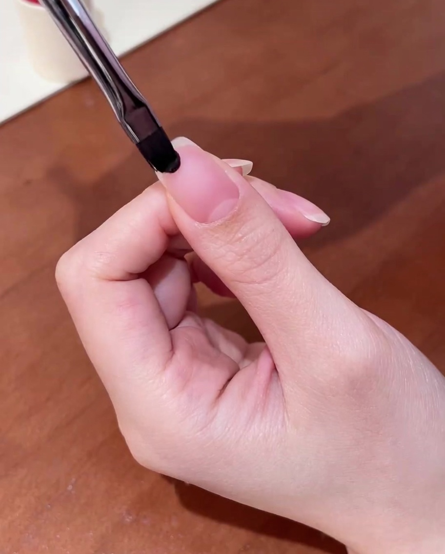 プレパレーション済みの自爪にクリアのベースジェルを筆で塗布しているクローズアップ。