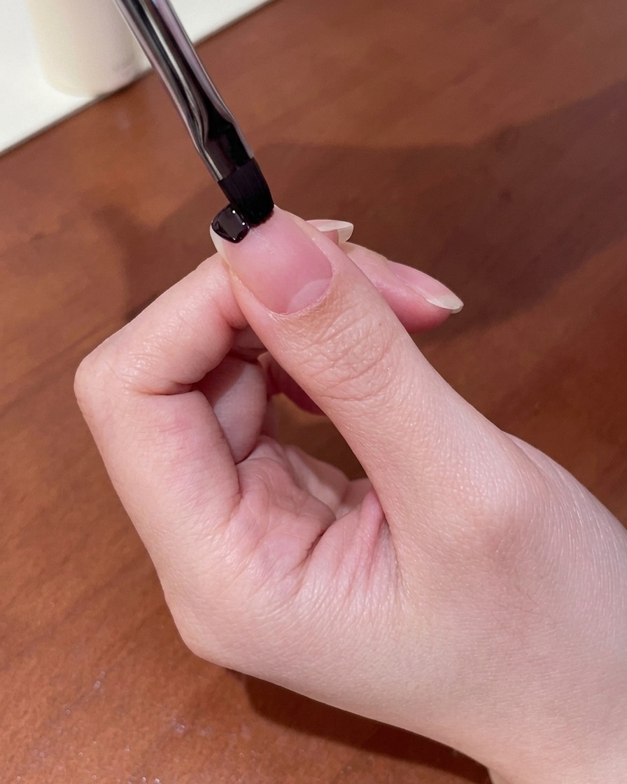 小さめのネイルブラシを使って、爪の先端にダークパープルのカラージェルを塗っている様子。