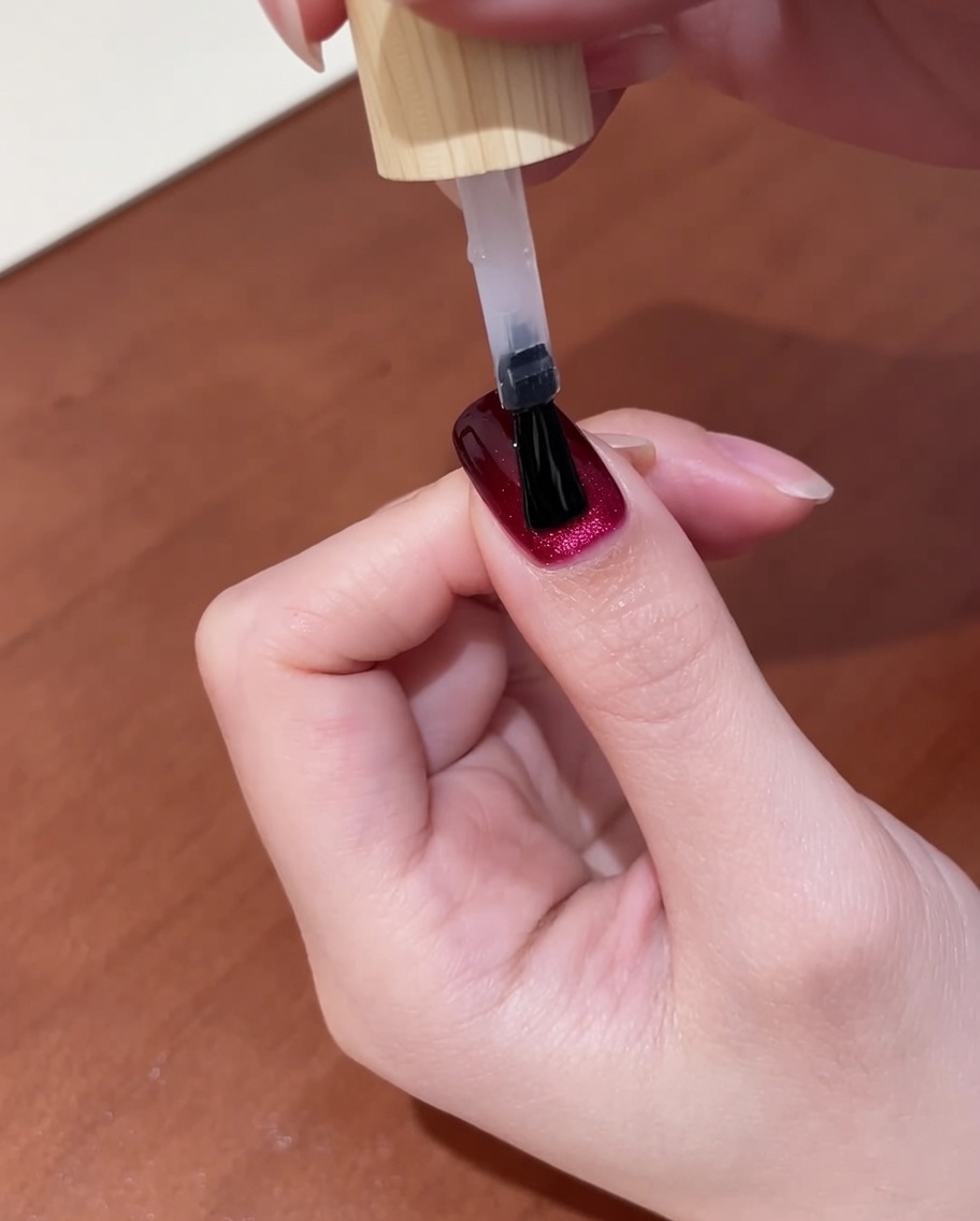 ダークレッドのキャッツアイネイルにトップコートを塗ったばかりの手を、最終硬化のためにUVネイルライトに入れているクローズアップ。