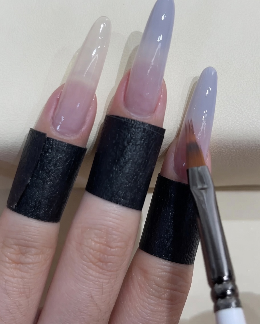 細いネイルブラシで爪の先端にさらにグレーブルーのジェルを塗り重ねている様子。