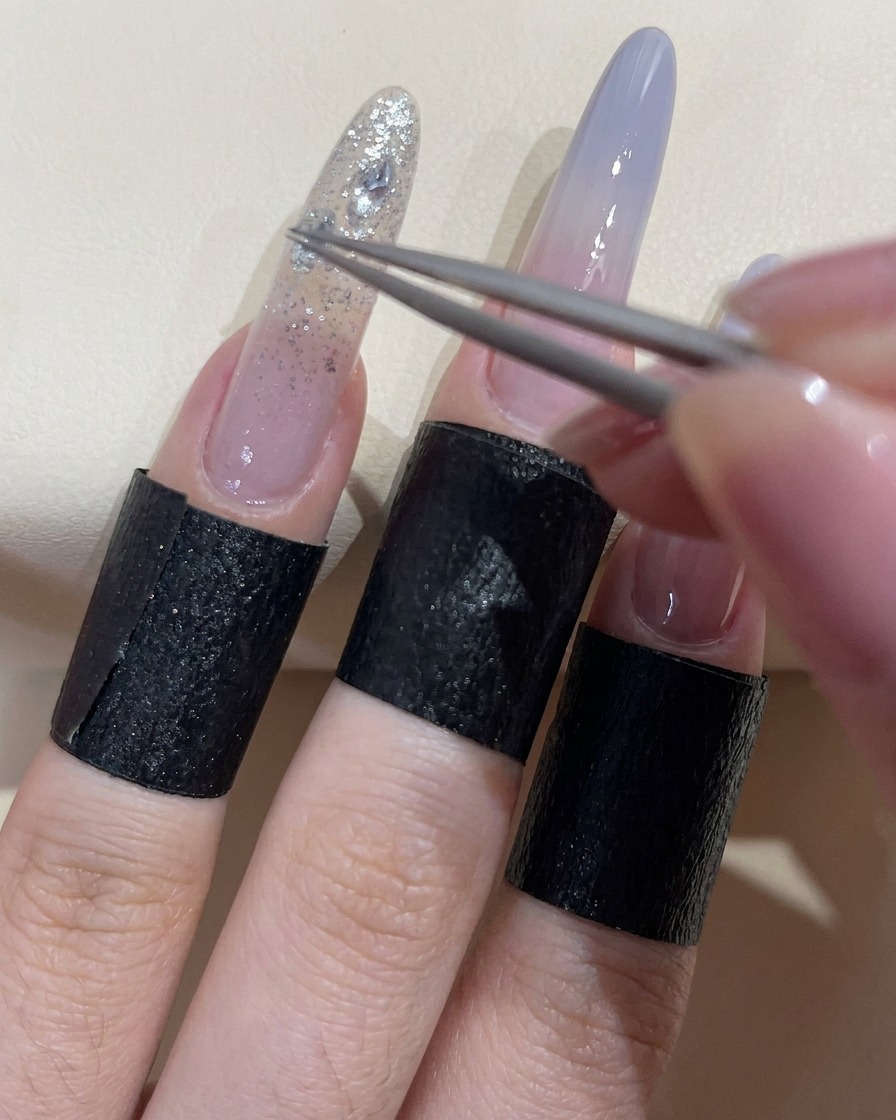 ピンセットで透明に輝くラインストーンをつまみ、固定用ジェルの上に配置している様子。