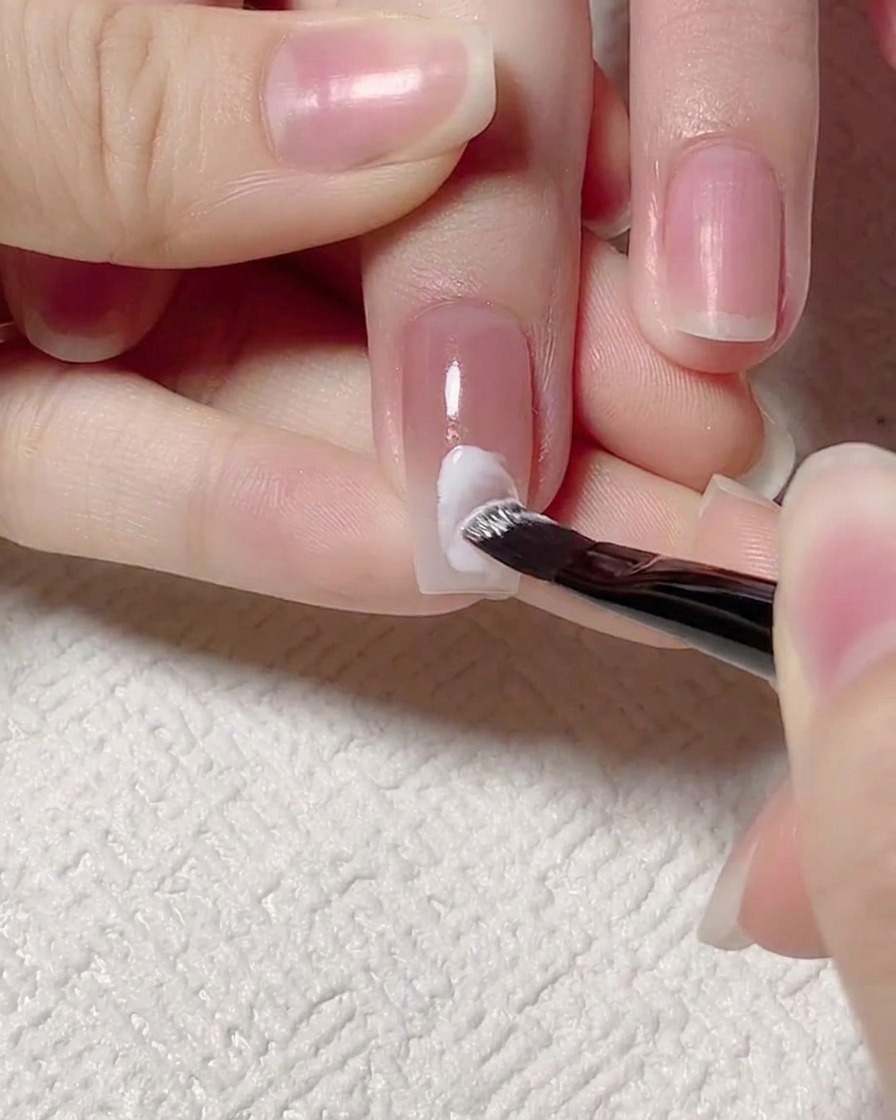 細筆を使い、ホワイトジェルでネイルの中央に水の波紋のようなラインを描いている様子。