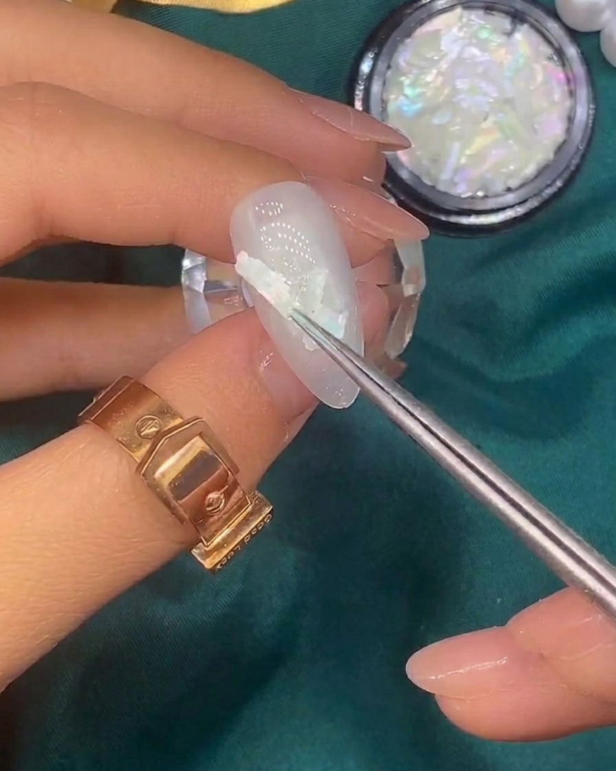 シェルを乗せたネイルに筆で金箔を散らしている様子