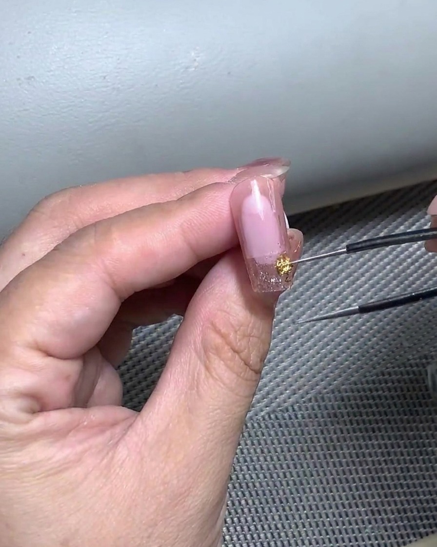 ピンセットを使い、カーブ状のフレンチネイルシールを爪に慎重に貼っているクローズアップ。
