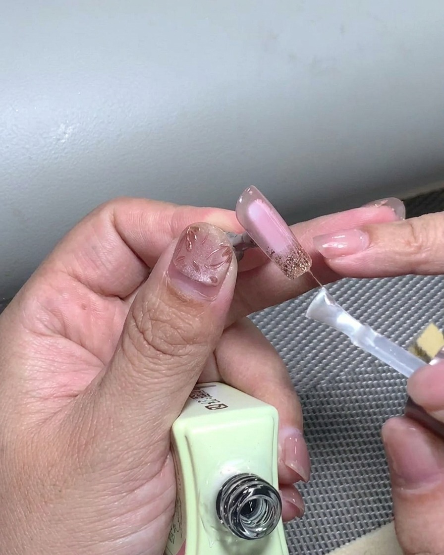 完成したフレンチデザインの爪全体にクリアなトップコートを塗布している様子。