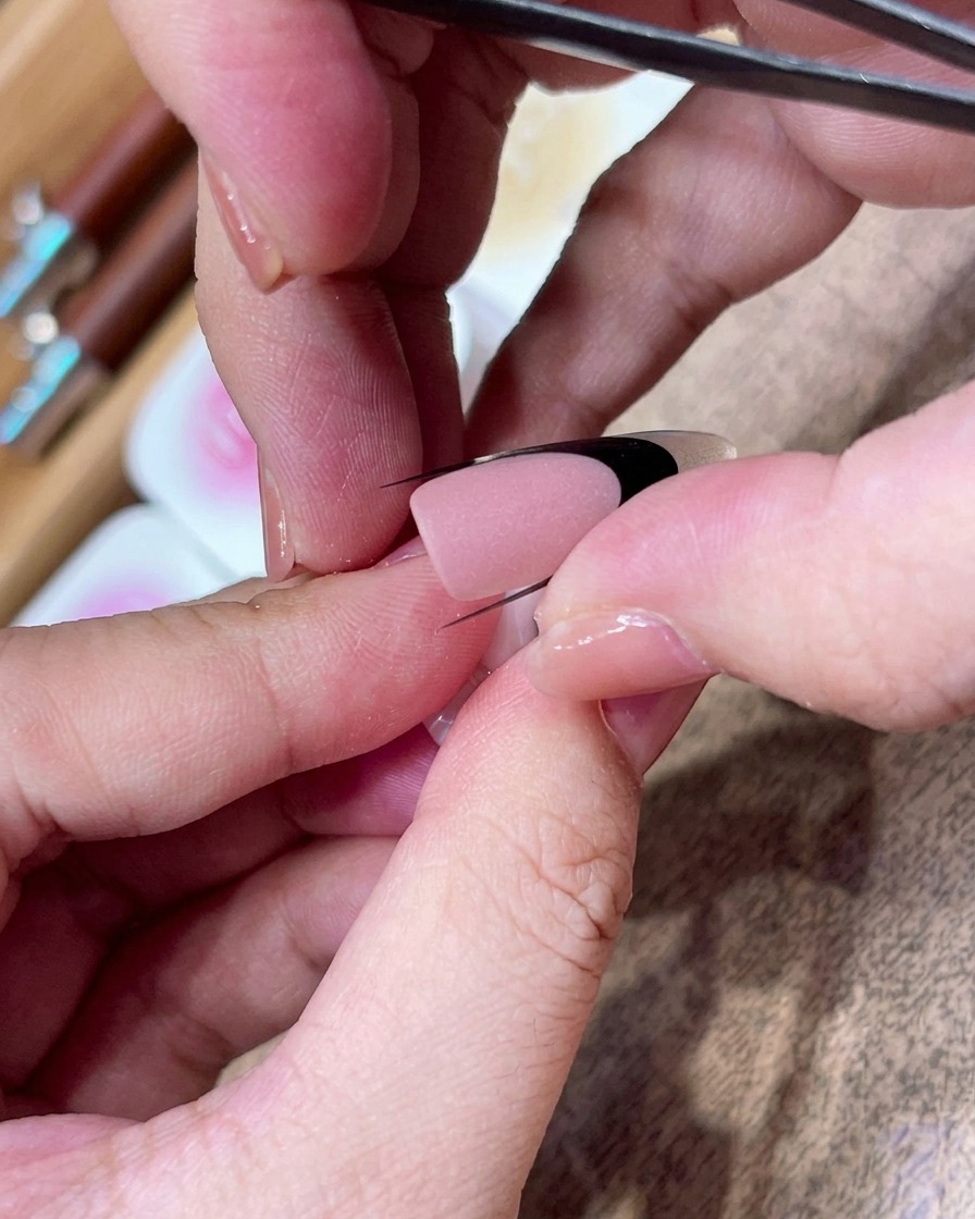 ピンセットを使って、マット仕上げのネイルに黒いカーブ状のガイドシールを斜めに慎重に配置している様子。