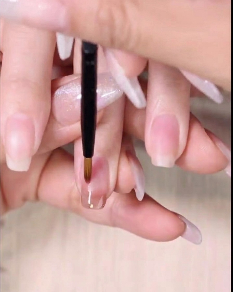 細筆で濡れた琥珀色のジェルの境目を下にぼかしてグラデーションにしている様子。