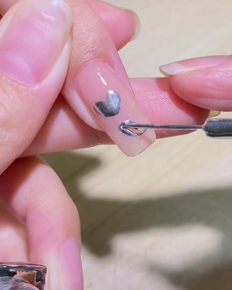 ネイルに描かれたシルバーのハートの輪郭の内側を筆で塗りつぶす様子。