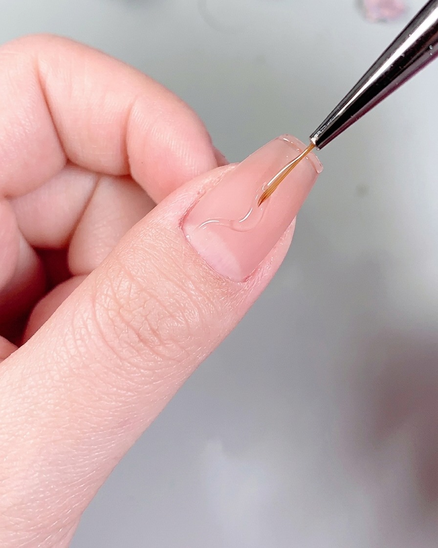 細いライナーブラシを使い、マットな爪の上にネイルグルーで繊細な炎の模様を描いている様子。