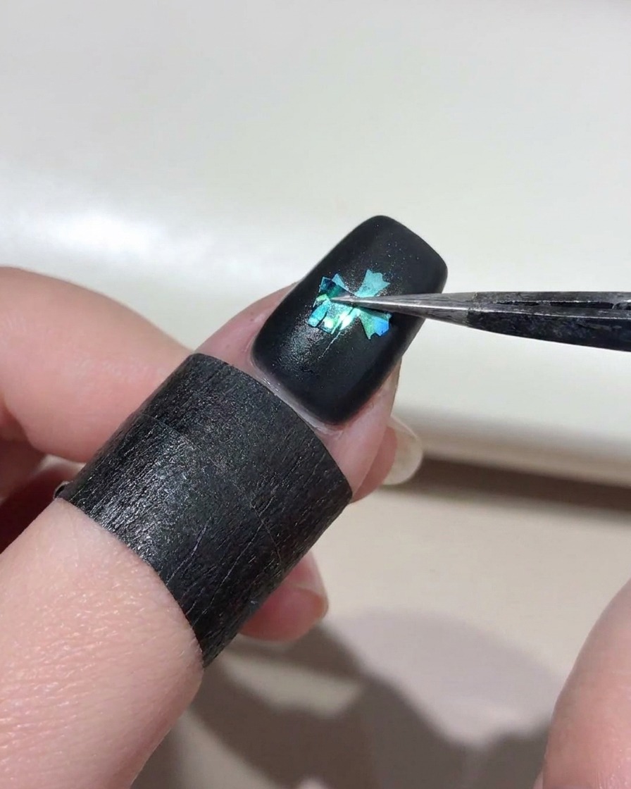 黒いジェルが塗られた爪から、ピンセットでクロスステッカーを剥がしている様子。
