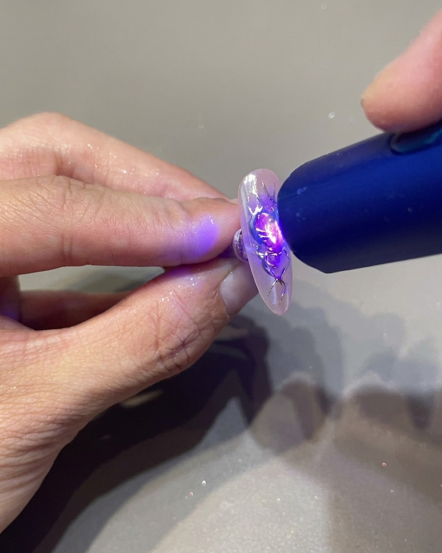 携帯用UVランプを爪に近づけ、3Dジェルを完全に硬化させている様子。
