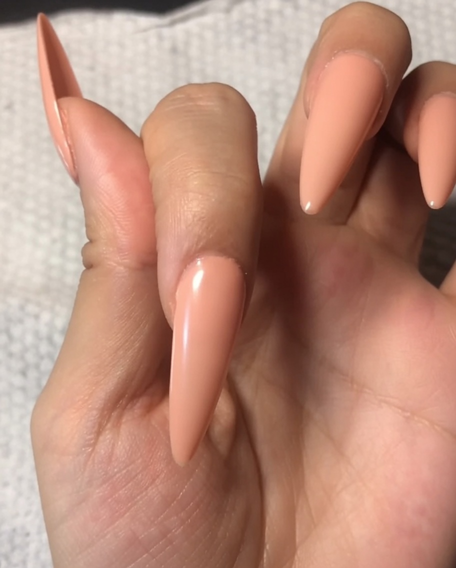 ヌードカラーで彩られた爪に、透明で艶やかなトップコートを塗布している様子。