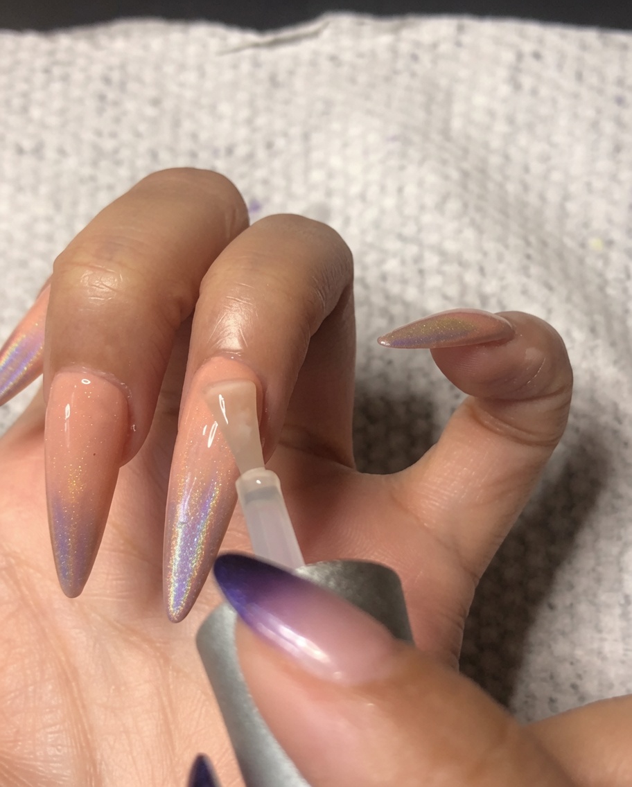 薬指に仕上げのトップコートを塗り、ネイルアートを保護している様子。