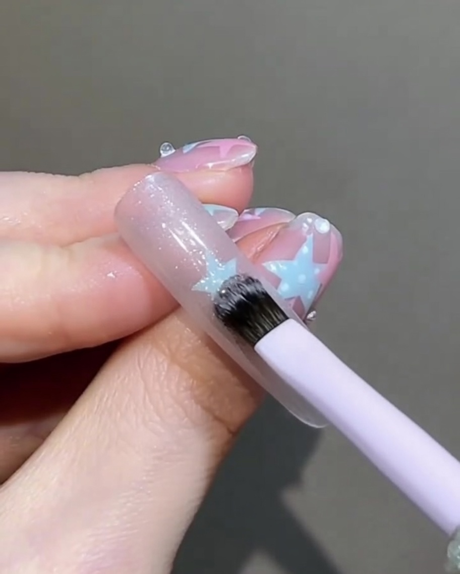 小さなフラットブラシで、爪の上の濡れたマグネットジェルを優しく叩いて均一に整えている様子。