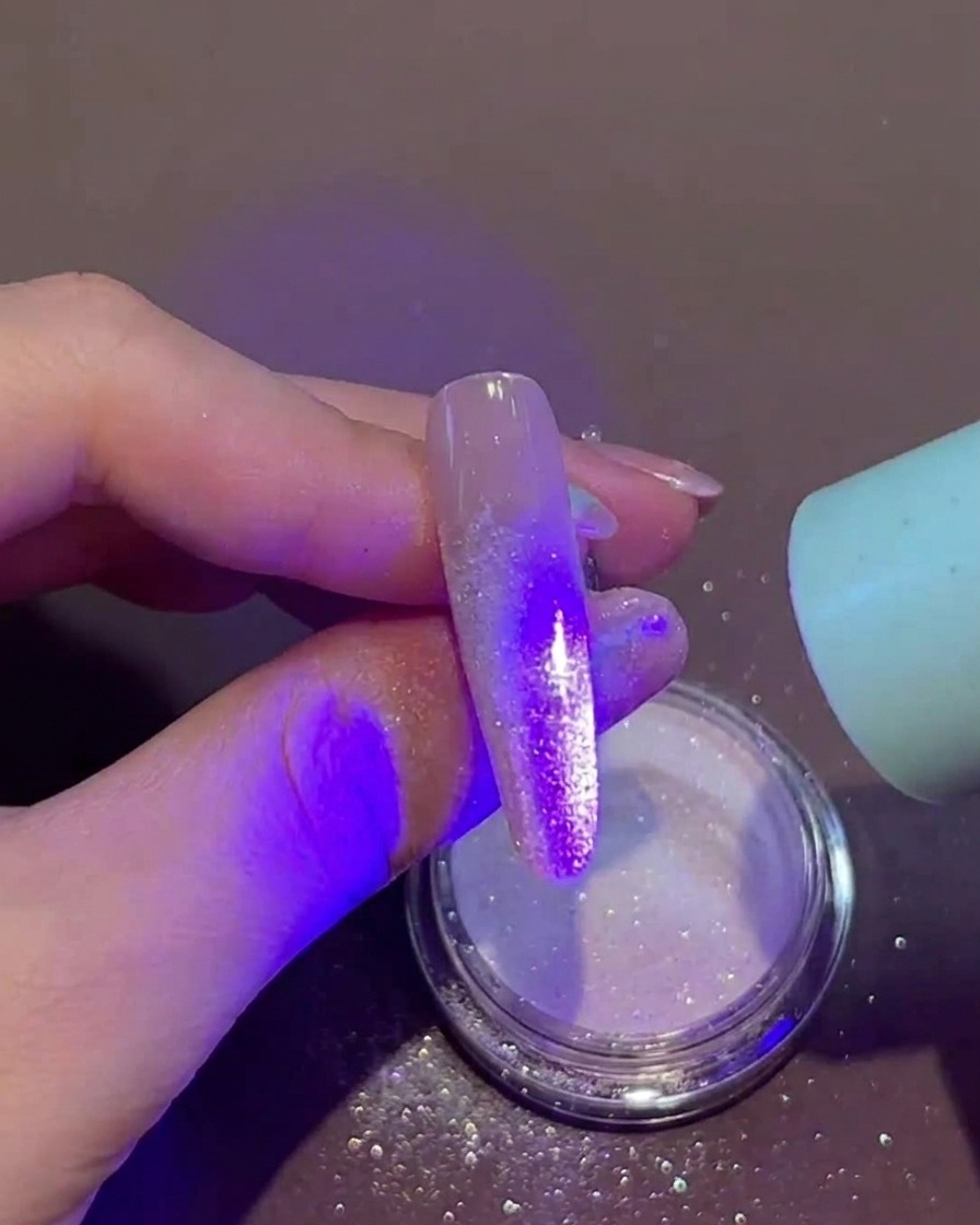 ジェルとパウダーがついた爪に、手持ちの小型UV/LEDランプを近づけて硬化させている様子。