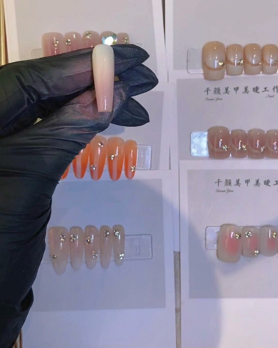 エアブラシで塗装されたネイルの根本に、ピンセットで小さな輝くクリスタルを置いている様子。