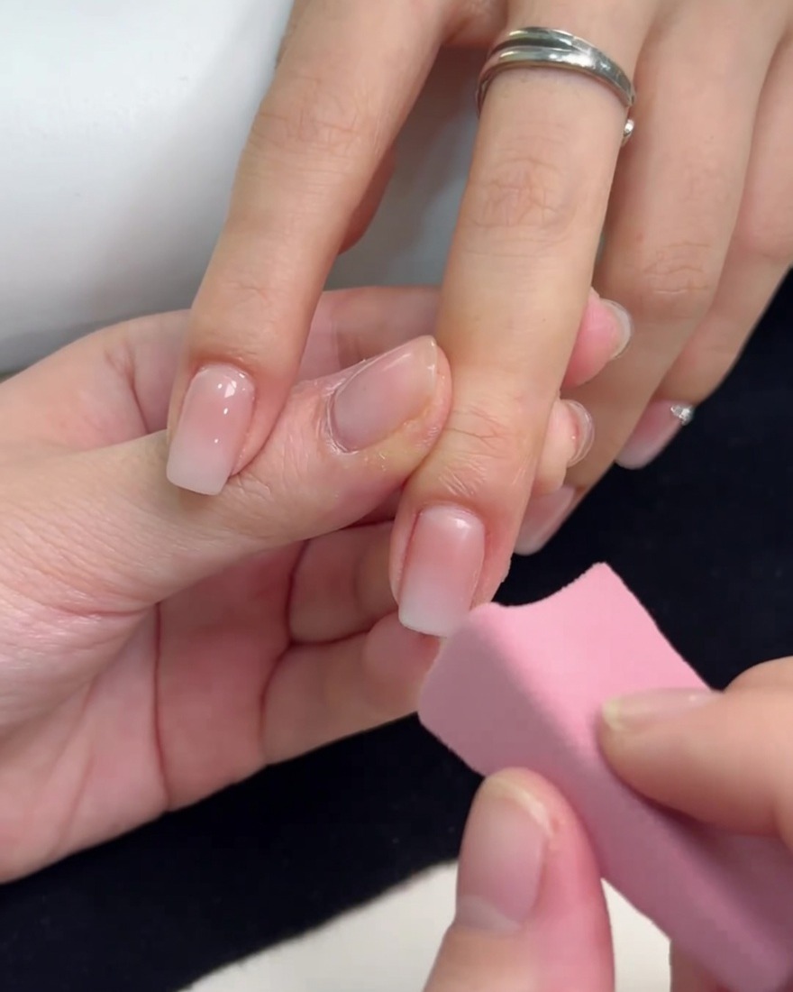 小さなピンクのスポンジで、爪先にホワイトジェルを重ねてグラデーションの深みを出している様子。