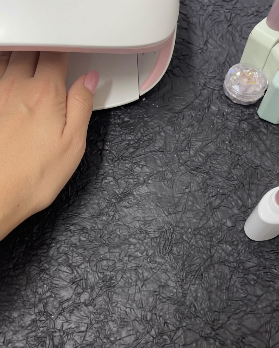 A hand placed inside a white UV/LED nail lamp for curing.