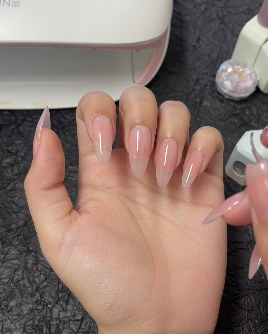 A brush applying a second layer of nude gel polish to a thumb.