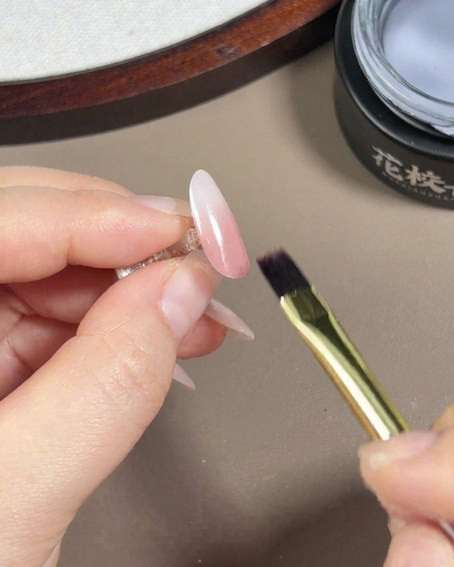 完成したグラデーションネイルに、ツヤのあるトップコートを塗っている様子。