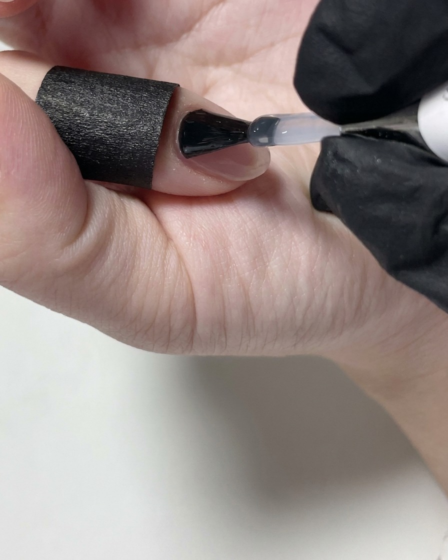 ヌードカラーのネイルの上にマットトップコートを塗っている様子。