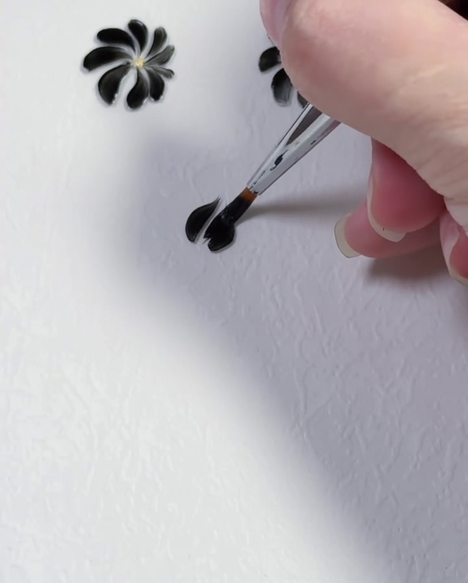 白い背景の上で、細いライナーブラシを使って2枚目の黒いジェルの花びらを描いている様子。