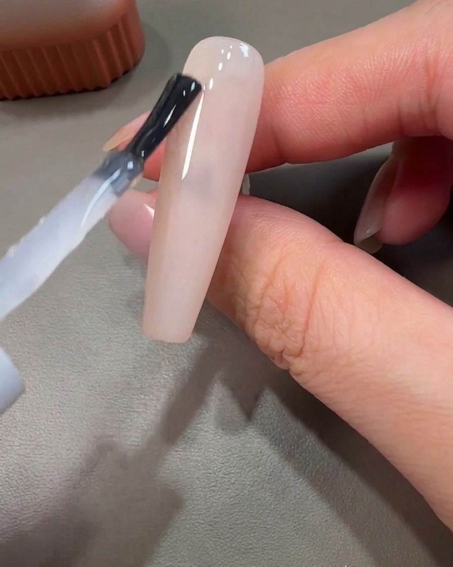 未硬化のベースの上に、細筆でピンクのジェルを円を描くように乗せているクローズアップ。