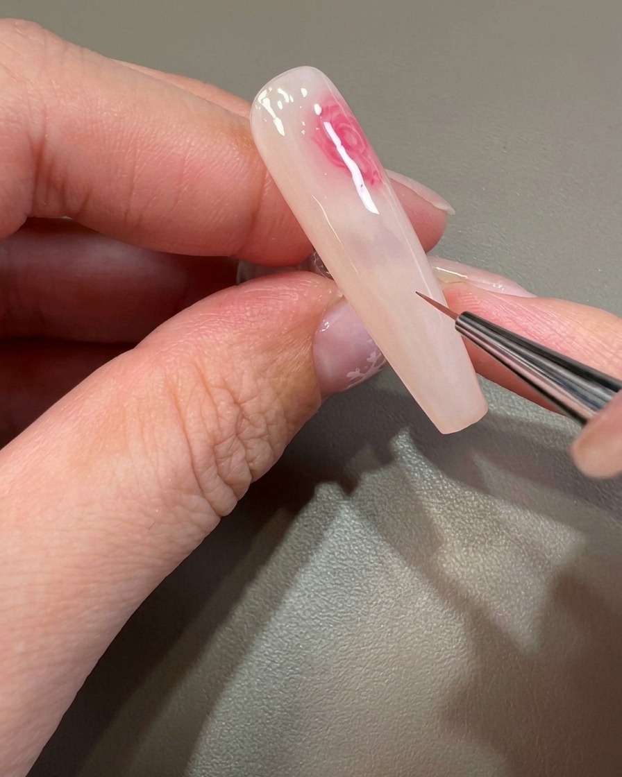 爪の上に広がるピンクのふんわりとした模様を、細筆で繊細に調整している様子。