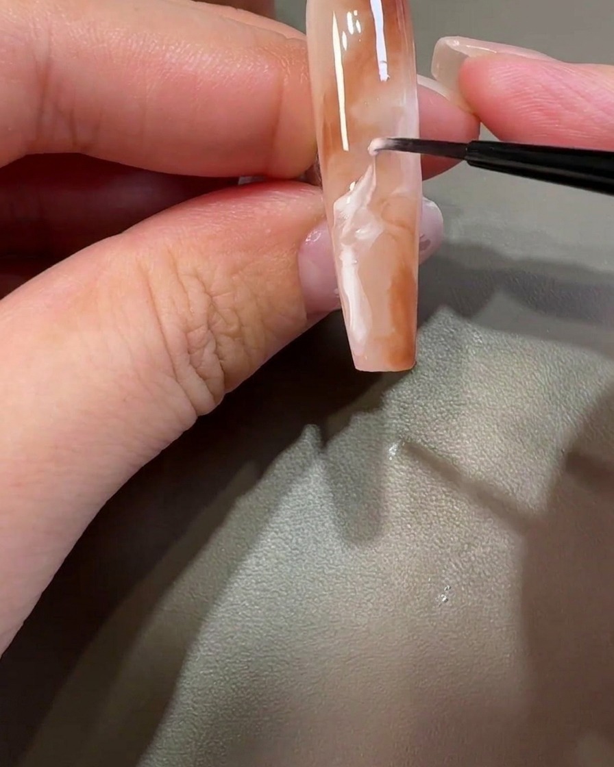 細筆でホワイトジェルを周囲のブラウンに馴染ませ、雲のようなマーブルを作っている様子。