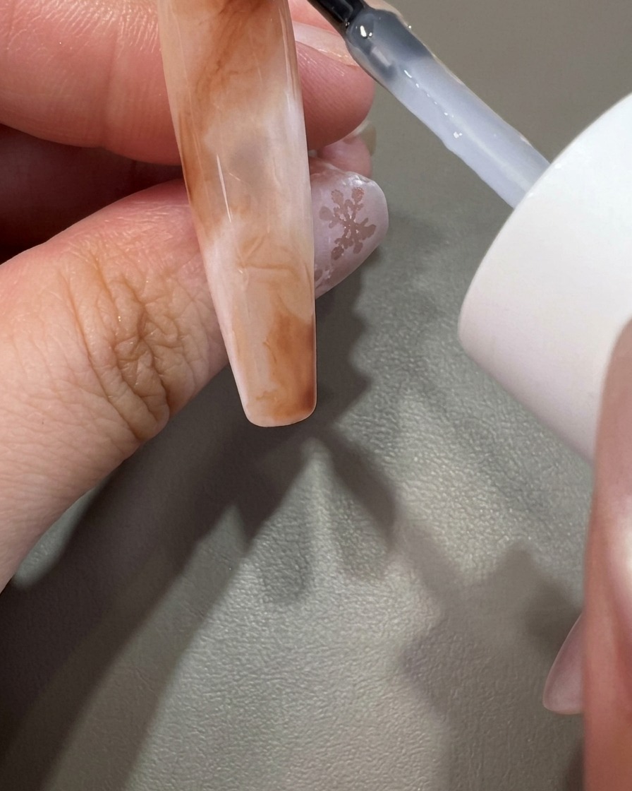 完成したマーブルネイルの上に、透明なトップコートを塗布している様子。