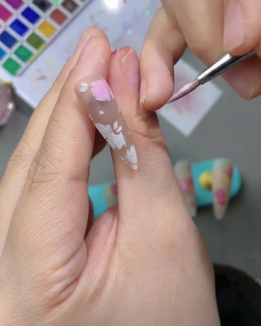 細いネイルアート筆を使い、淡いピンクの水彩絵の具で花びらの形を塗り込んでいる様子。